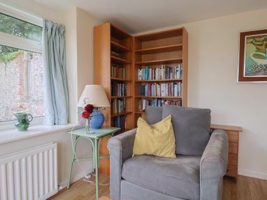 A living room with an armchair and bookshelf at Penny Plot Cottage in Lyme Regis