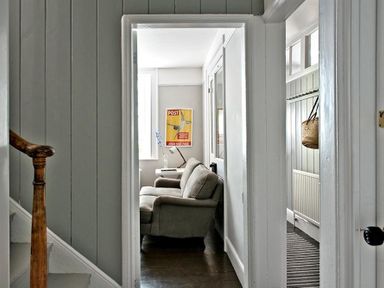 A hallway with a staircase and doorway leading to a room with a sofa and side table with a lamp at The Arched House in Lyme Regis