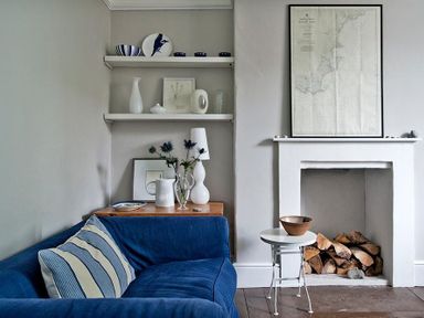 A living room with a blue sofa and shelves above a wooden side table next to a fireplace with firewood at The Arched House in Lyme Regis