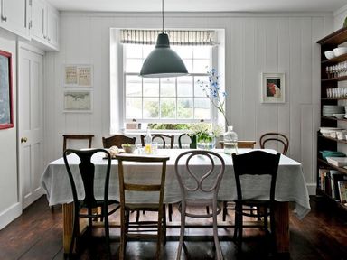A dining room with a large table and mixed chairs by a window at The Arched House in Lyme Regis