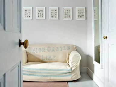 A small sofa with a cover reading Union-Castle Line below five framed prints on a wall at The Arched House in Lyme Regis