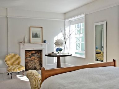 A bedroom with a wooden bed a round table with flowers a fireplace and a yellow striped chair at The Arched House in Lyme Regis