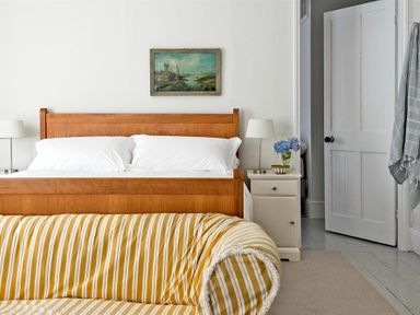 A bedroom with a wooden bed frame white pillows bedside tables lamps a painting above the bed and a striped sofa at The Arched House in Lyme Regis