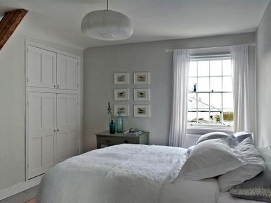 A bedroom with a bed near a window and a dresser with bottles and framed pictures on the wall at The Arched House in Lyme Regis
