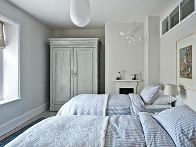 A bedroom with two beds a wardrobe a small fireplace and framed bird artwork at The Arched House in Lyme Regis