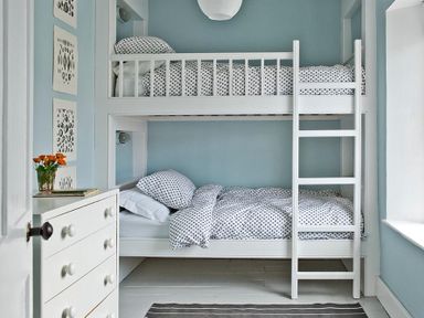 A small bedroom with white bunk beds and polka dot bedding a white dresser with flowers and wall art at The Arched House in Lyme Regis