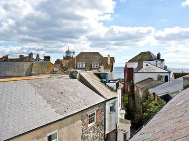 Rooftops of houses with chimneys under a partly cloudy sky facing the sea at The Arched House in Lyme Regis