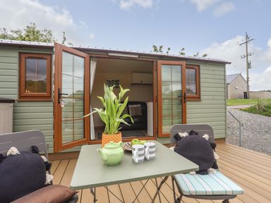 An outdoor patio with table and chairs in front of a small cabin with open double doors at Llety'r Bugail 2 in Llanrug
