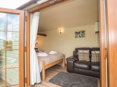 A bedroom with a wooden bed and a leather sofa with cushions at Llety'r Bugail 2 in Llanrug