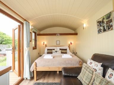 A bedroom with a wooden bed and brown pillows next to a brown leather sofa with cushions at Llety'r Bugail 2 in Llanrug