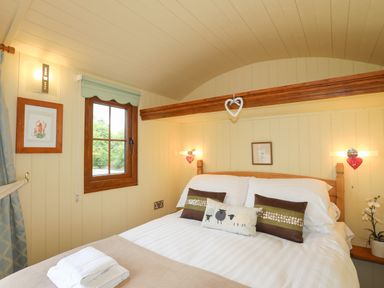 A bedroom with a double bed pillows a window and framed pictures at Lletyr Bugail 2 in Llanrug