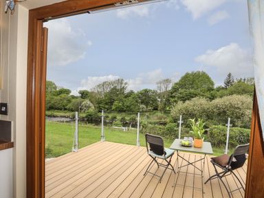 A balcony with a table and two chairs overlooking a grassy area and trees at Llety'r Bugail 2 in Llanrug