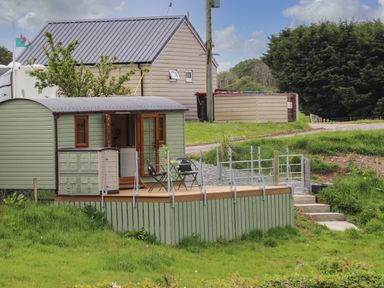 A small green cabin with a wooden deck and outdoor chairs in a grassy area at Llety'r Bugail 2 in Llanrug