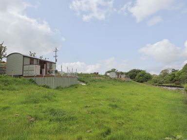 Two small cabins on raised platforms with grassy field and trees surrounding them at Llety'r Bugail 2 Llanrug