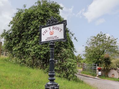 A metal signpost with the text Cil y Bont Caravan and Motorhome Club by a country road with trees and grass at Llety'r Bugail 2 Llanrug