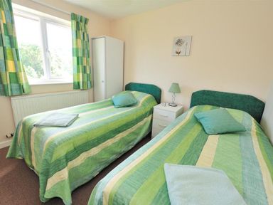A bedroom with two single beds with green striped bedspreads a white wardrobe and a bedside table with a lamp at Bridge House Apartment in Charmouth