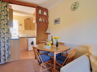 A dining area with a round wooden table and four chairs next to a kitchen at Bridge House Apartment in Charmouth