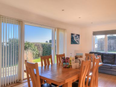 A dining area with a wooden table and chairs next to sliding glass doors with a view of a garden at Pendower in Charmouth