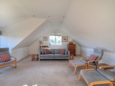 An attic living room with a sofa armchairs footstools side tables and a chest of drawers at Pendower in Charmouth