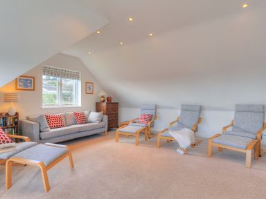 A sitting room with a sofa, armchairs, ottomans, a window, a chest of drawers, a lamp, and framed pictures at Pendower in Charmouth