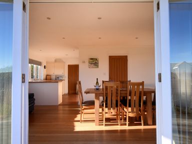 A dining area with wooden table and chairs and kitchen in the background at Pendower in Charmouth