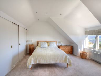 A bedroom with a bed centered between two wooden bedside tables with lamps and a window with a view at Pendower in Charmouth