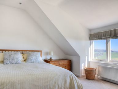 A bedroom with a bed two pillows a bedside table with lamp a wooden chest a window and a wicker basket at Pendower in Charmouth
