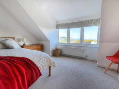 A bedroom with a bed a wooden chest a basket a red chair and a window with a view at Pendower in Charmouth