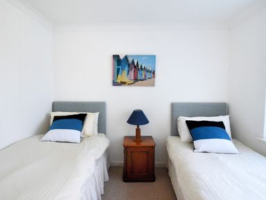 A bedroom with two single beds a wooden bedside table with a lamp and a colorful wall picture at Pendower in Charmouth