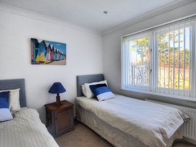 A bedroom with two single beds a bedside table with a lamp and a window with vertical blinds at Pendower in Charmouth