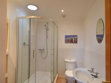 A bathroom with a glass shower enclosure toilet sink round mirror and colorful artwork at Pendower in Charmouth