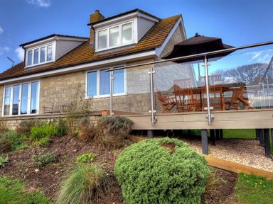 A house with a stone exterior and a raised deck with wooden furniture and a black umbrella at Pendower in Charmouth