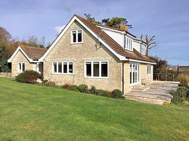 A stone house with multiple windows and a patio surrounded by a lawn at Pendower in Charmouth
