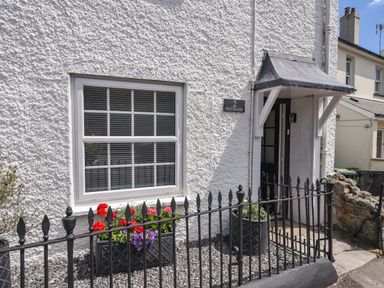 The front entrance of a white textured wall house with a window, flower boxes, and a black iron fence at Nutwood in Charmouth