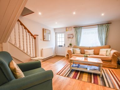 A living room with a green armchair a beige sofa a wooden coffee table and a striped rug at Nutwood in Charmouth