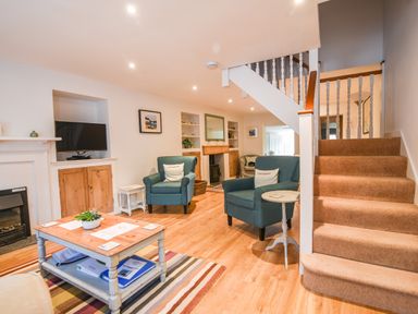 A living room with two blue armchairs a wooden coffee table a fireplace a TV and carpeted stairs at Nutwood in Charmouth