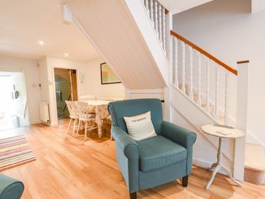 A living area with a blue armchair a small round table a dining table with chairs and a staircase in Nutwood Charmouth