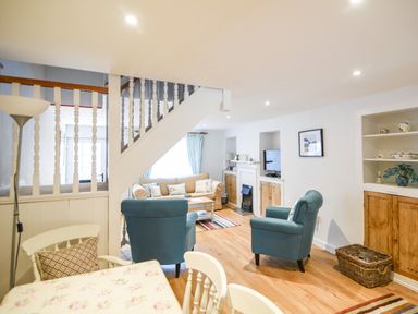 A living room with blue armchairs a beige sofa and a dining table with floral cover at Nutwood in Charmouth