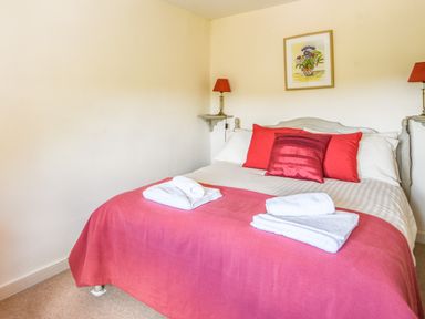 A bedroom with a bed covered with a red blanket and red pillows with folded white towels on the bed at Nutwood in Charmouth