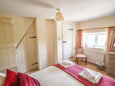 A bedroom with a bed, wooden chair, small window with curtains, a chest of drawers, and two small wooden doors at Nutwood in Charmouth