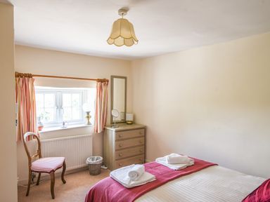 A bedroom with a bed covered with a red throw and white towels on it a wooden chair near a window with striped curtains and a dresser with a mirror at Nutwood in Charmouth