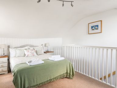 A bedroom with a bed with green throw and pillows between two bedside tables with lamps at Nutwood in Charmouth