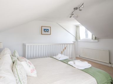 A bedroom with a bed set with pillows and towels near a window and a staircase at Nutwood in Charmouth