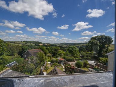 A view of a garden with a small gazebo a house a van and rolling hills under a blue sky at Nutwood in Charmouth