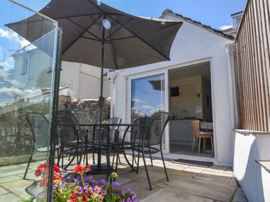 An outdoor patio with a metal table and chairs under a large umbrella next to a building with sliding glass doors at Nutwood in Charmouth