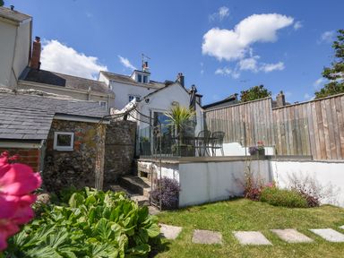 A garden with plants steps and a patio area with a table and chairs at Nutwood in Charmouth