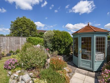 A garden with shrubs flowers and a wooden gazebo with glass windows and a tiled roof at Nutwood in Charmouth
