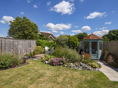 A garden with a small greenhouse stone edging and a seating area at Nutwood in Charmouth