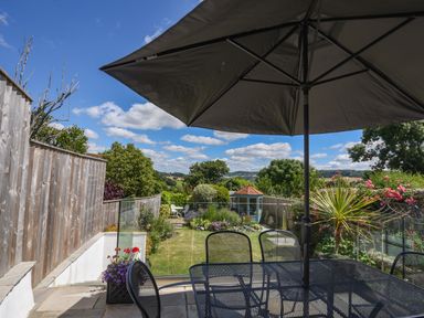 A garden with a table and chairs under an umbrella and a small gazebo in the background at Nutwood in Charmouth