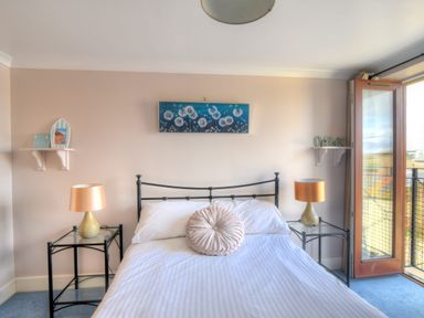 A bedroom with a double bed two bedside tables with lamps wall shelves and a balcony door at 9 Maritime House in West Bay